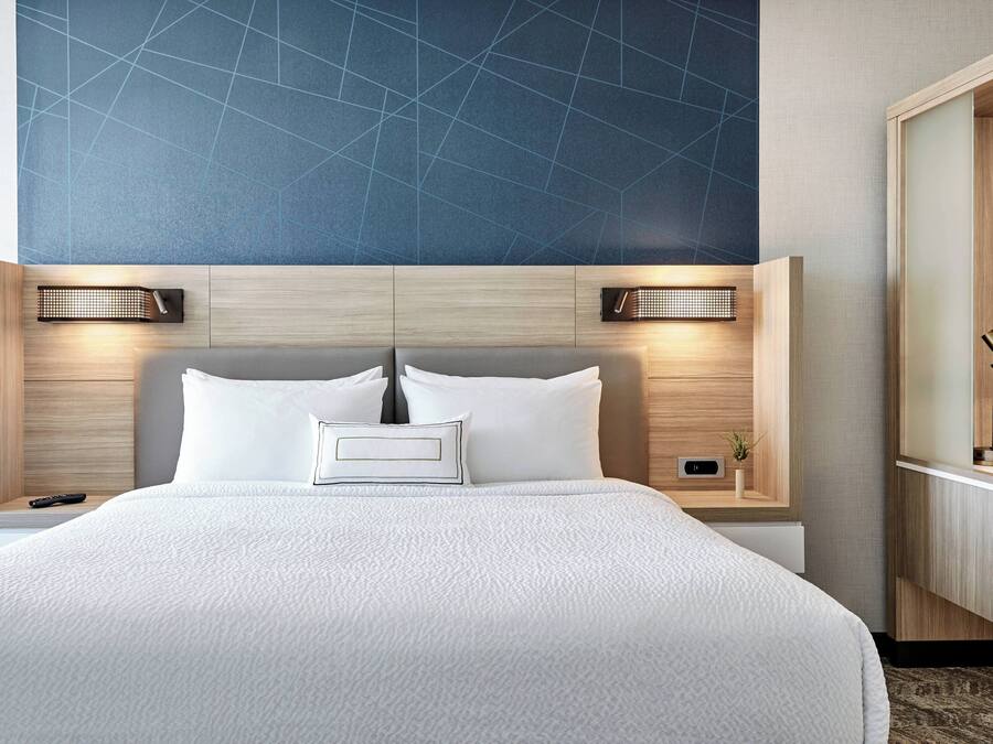 A modern hotel room with a large bed, two bedside tables, a nightstand, and a wooden wardrobe.