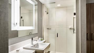 A modern bathroom with a large mirror, two sinks, and a walk-in shower.