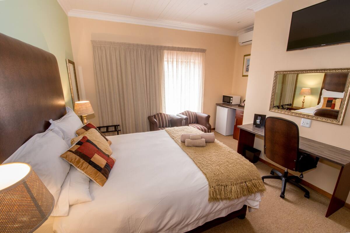 A hotel room with a large bed, a desk, a chair, a TV, and a mirror.