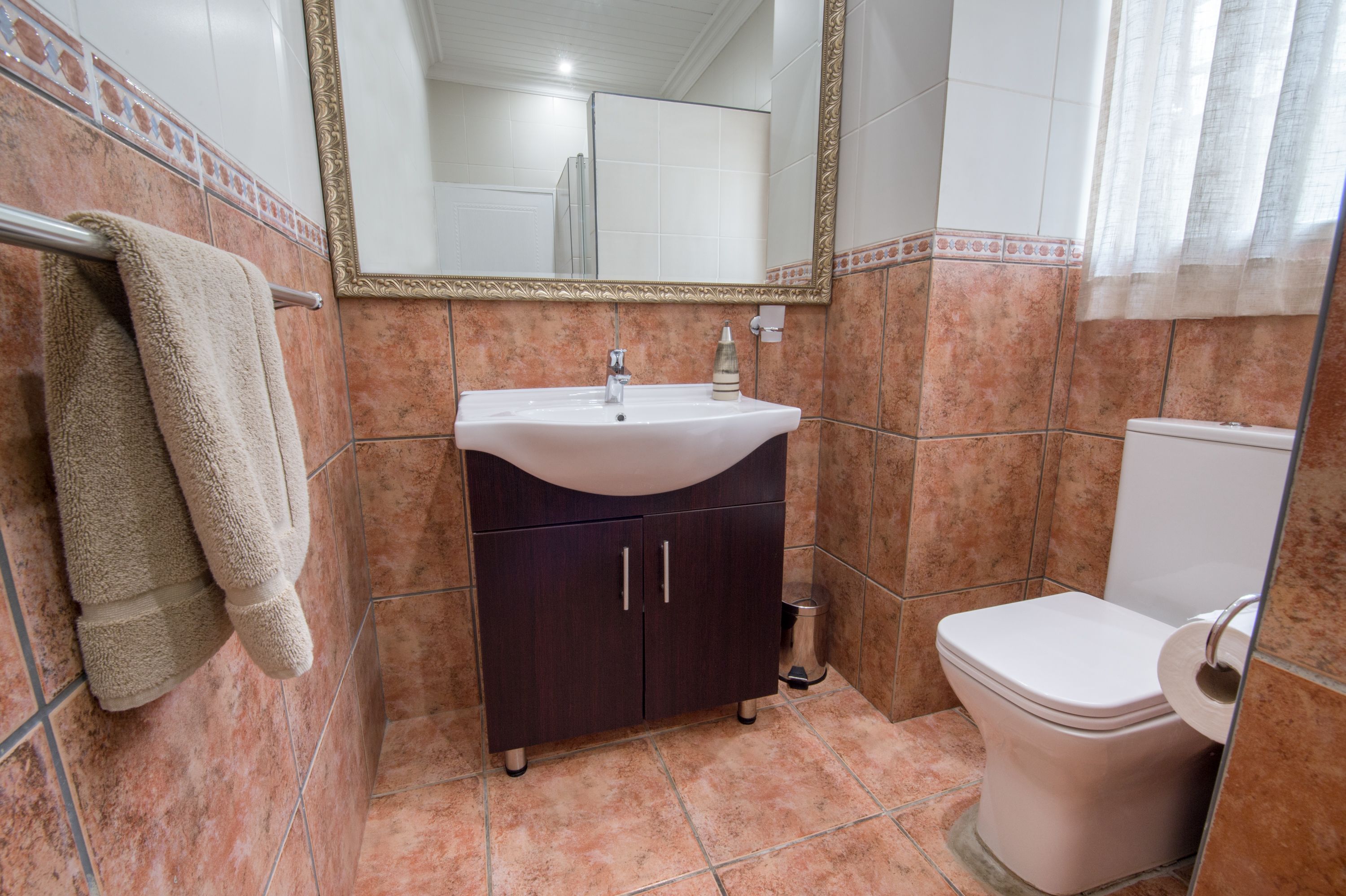 A bathroom with a sink, mirror, cabinet, toilet, and a trash can.