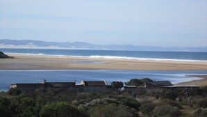 Une vue côtière avec une plage, quelques maisons et une chaîne de montagnes à l’horizon.