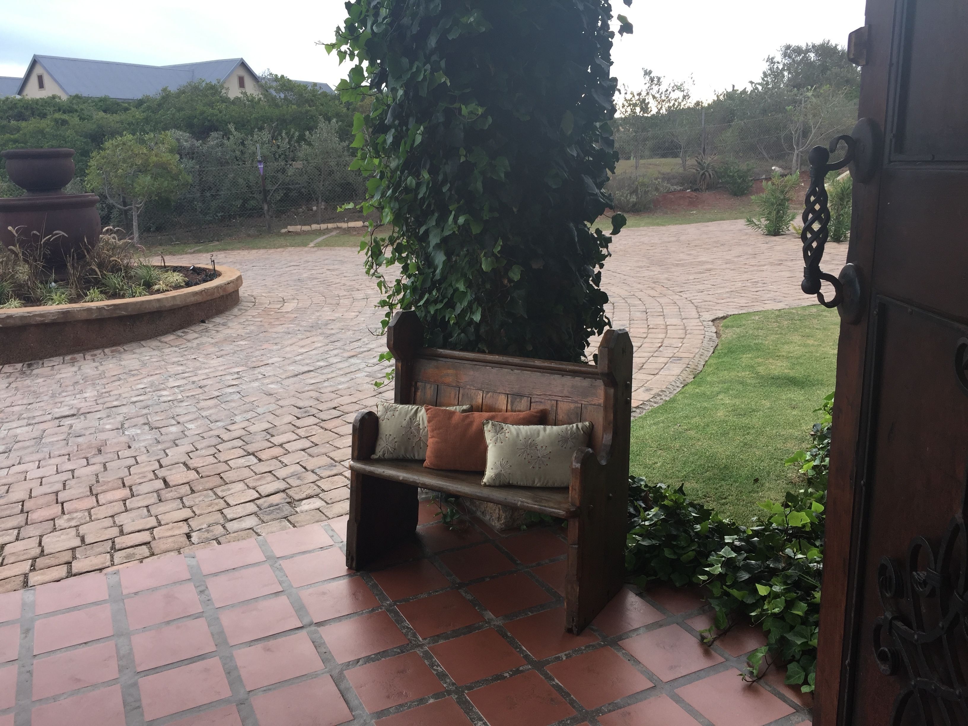 A bench with cushions in a garden area with a brick pathway.