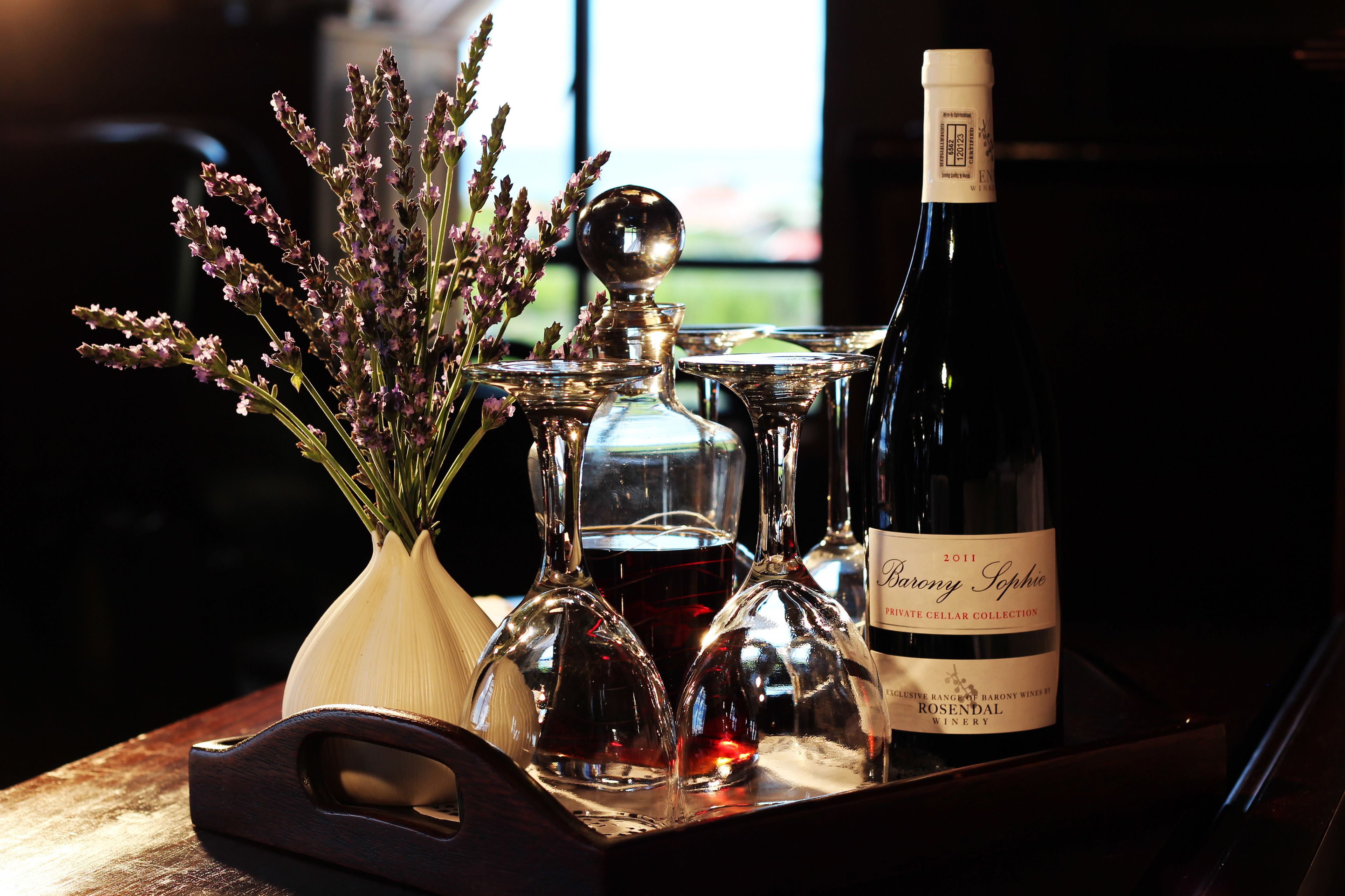 Una bandeja con una botella de vino, copas de vino y un florero con flores.