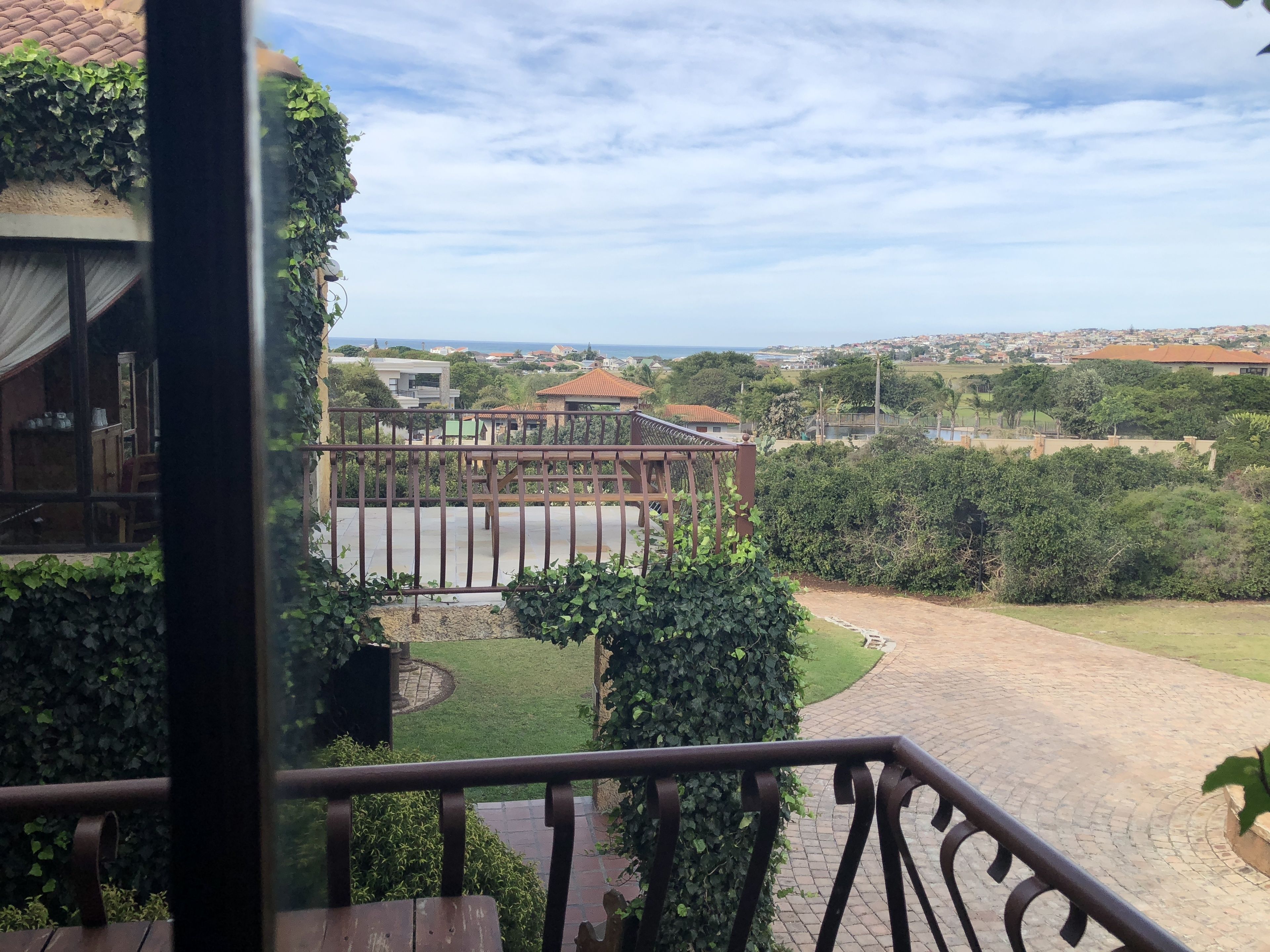 Vista desde un balcón sobre un jardín ajardinado con un sendero pavimentado, un pequeño jardín y edificios a lo lejos.