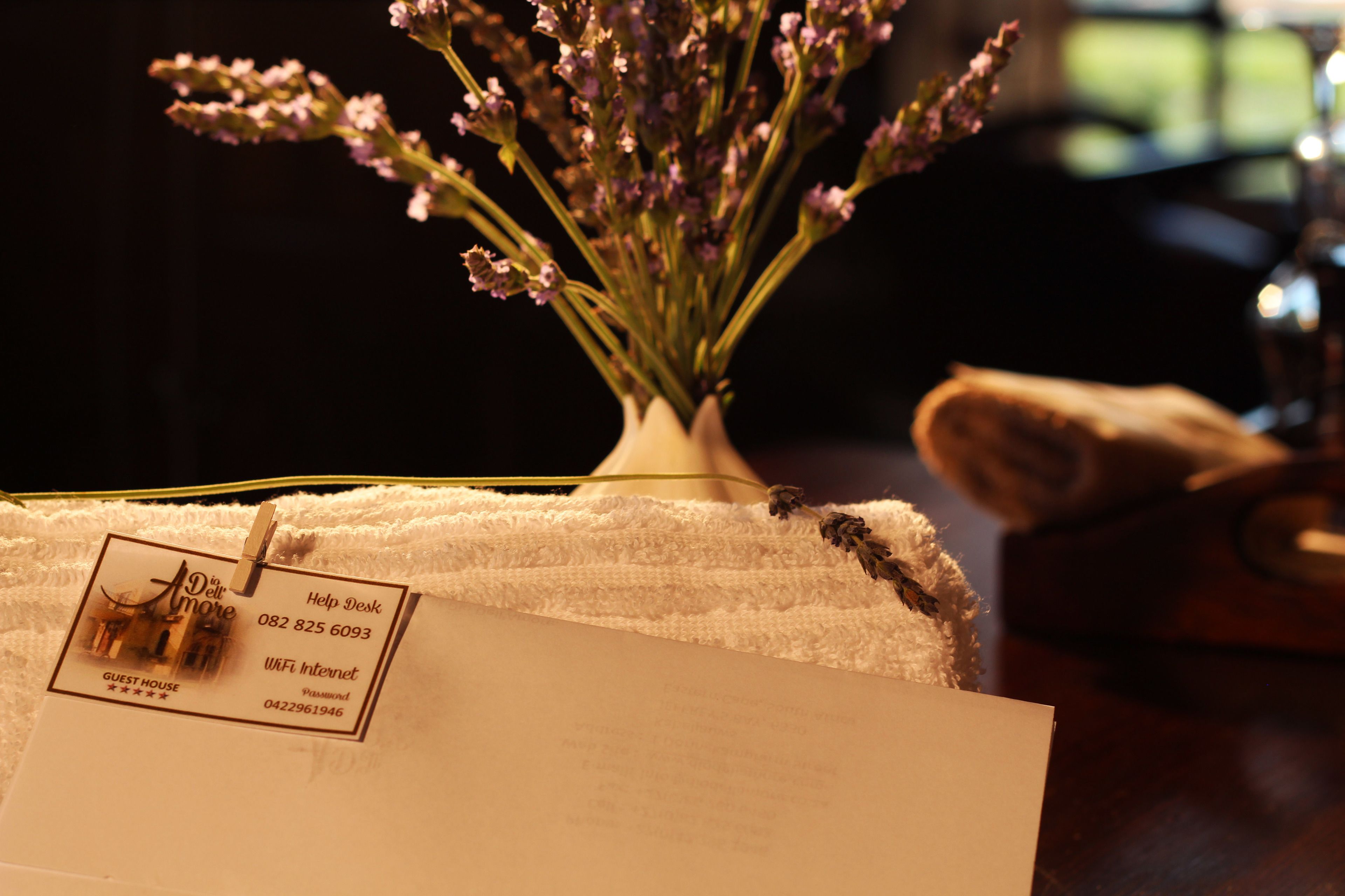 A white envelope with a hotel tag, a vase with lavender flowers, and a wooden table.