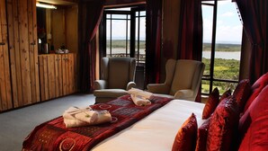 Une chambre d’hôtel avec un grand lit, deux fauteuils, une armoire en bois et une vue sur un lac.