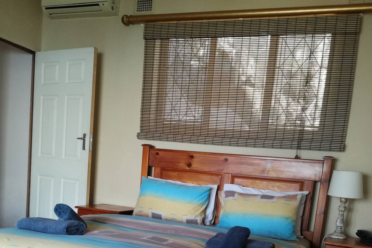A neatly made bed with a patterned bedspread, two pillows, and folded towels on a wooden headboard.