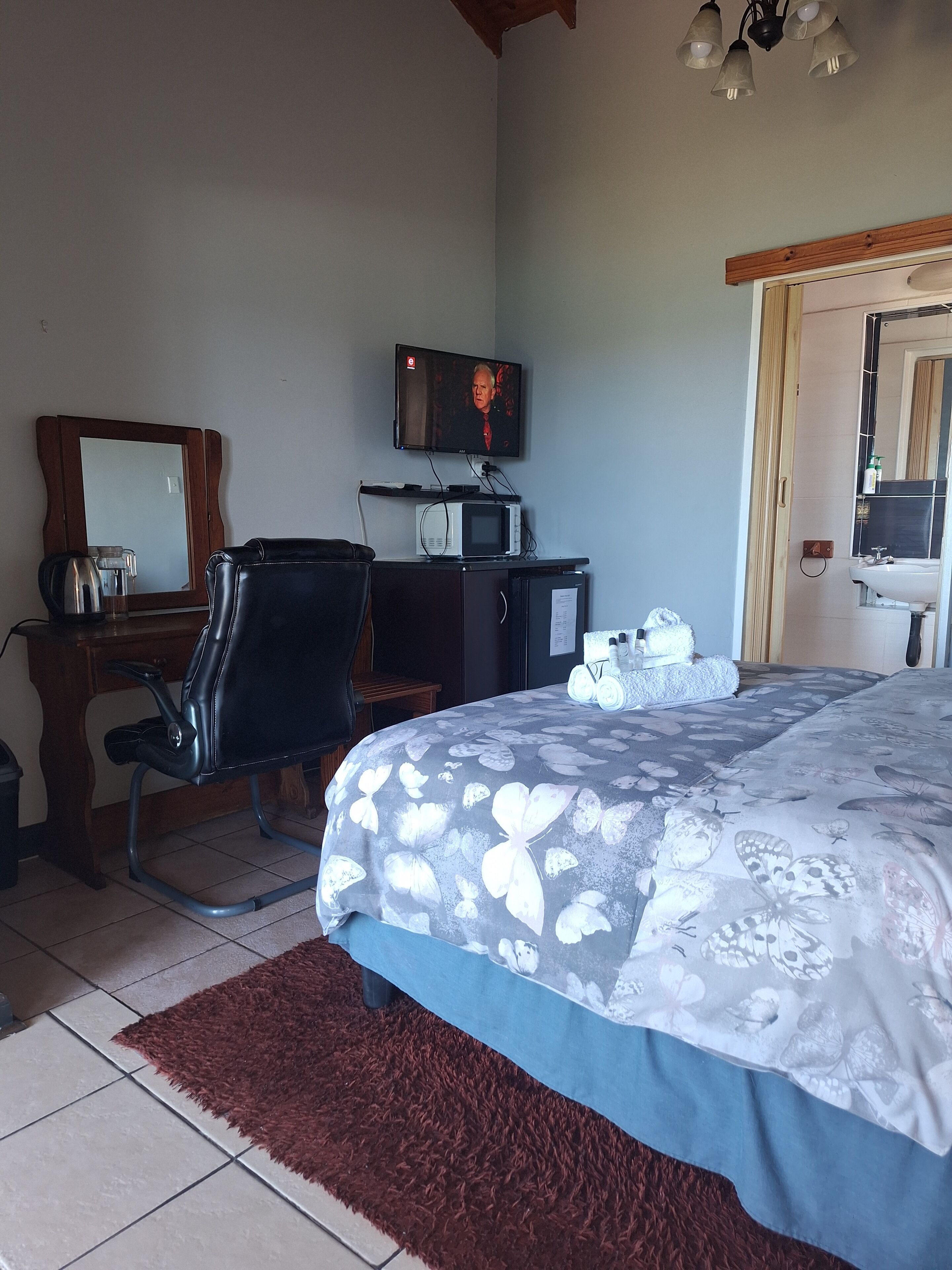 A hotel room with a bed, a desk with a chair, a television, a microwave, and a bathroom visible through an open door.