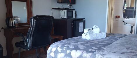 A hotel room with a bed, a desk with a chair, a television, a microwave, and a bathroom visible through an open door.