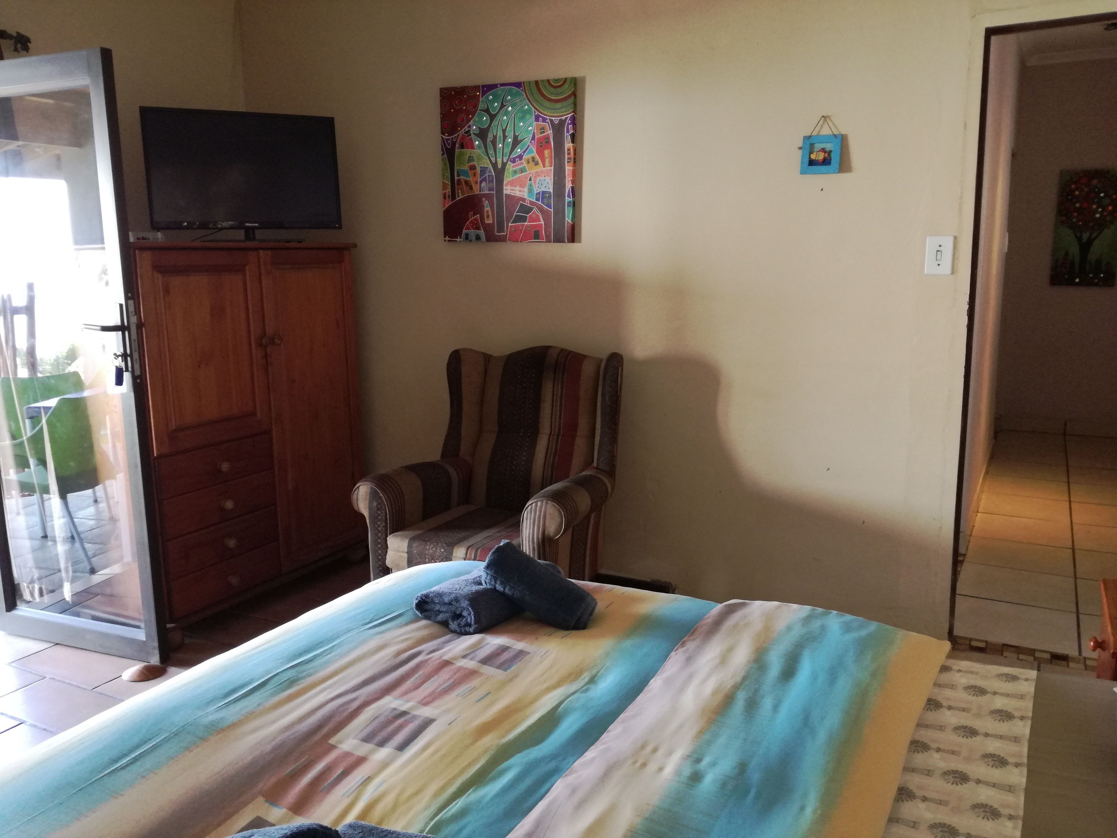 A bedroom with a bed, a chair, a television, and a painting on the wall.