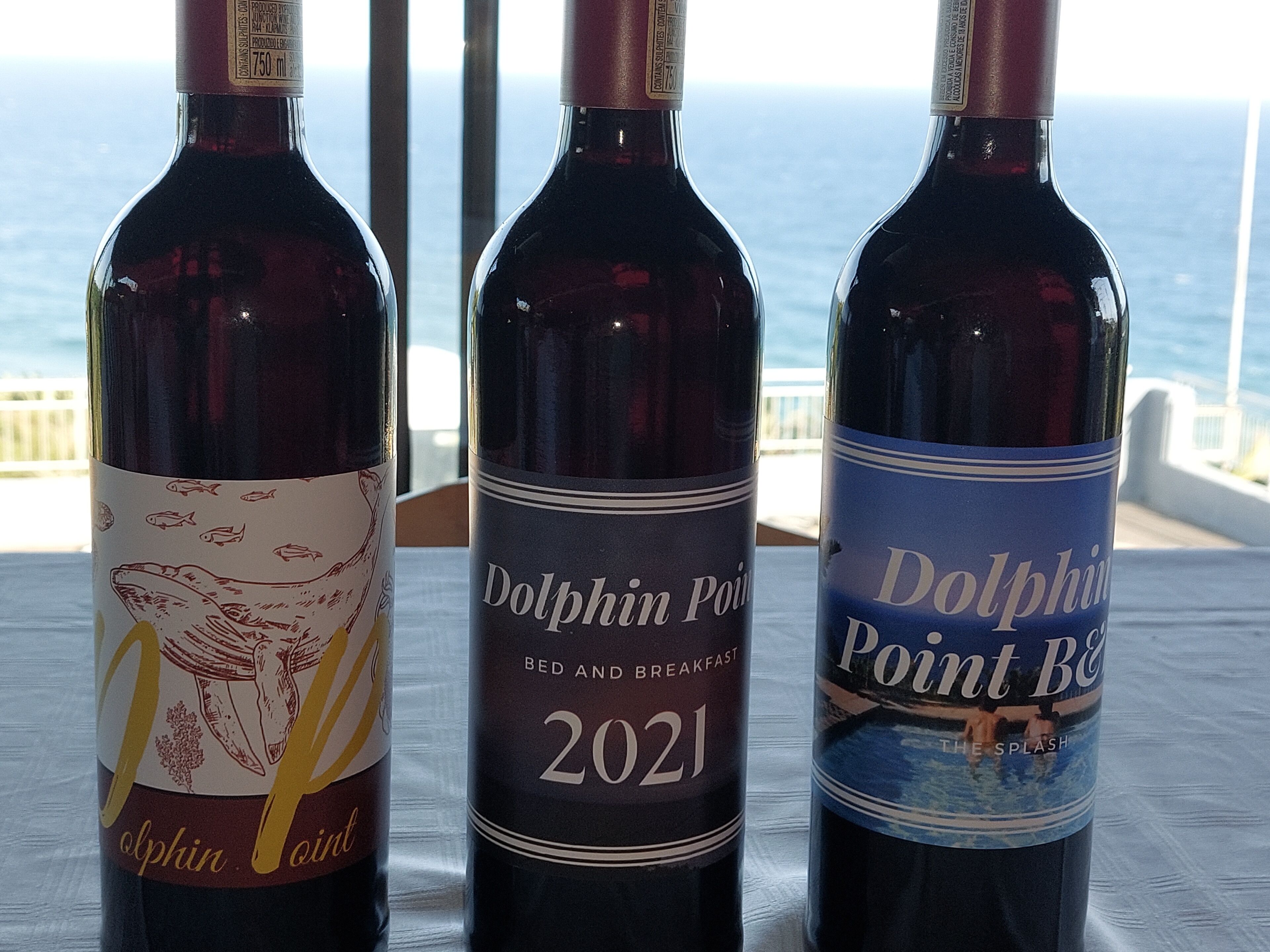 Three wine bottles on a table with a view of the ocean.