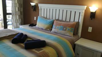 A neatly made bed with a striped blanket, two pillows, and rolled towels. There are two wall-mounted lights and a bedside table with a phone.