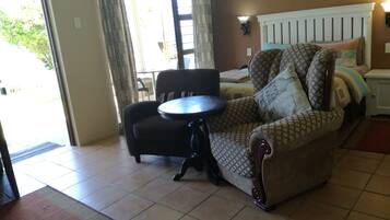 A room with a sofa, a small round table, a bed with patterned bedding, a nightstand, and a wall-mounted lamp.