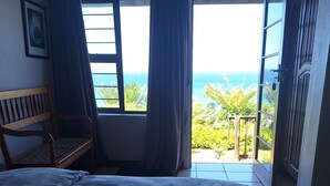 Un dormitorio con cama, un banco de madera y vista al océano a través de una ventana.