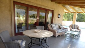 An outdoor patio area with wicker furniture, a round table, and a view of a pool and mountains. - Saddlebrook Cottage (Franschhoek)