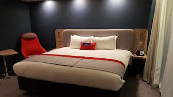 A modern hotel room with a large bed, a red chair, a bedside table with a phone, and a nightstand with a lamp.