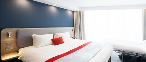A modern hotel room with a large bed, a bedside table, and a nightstand.