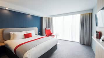 Una habitación de hotel con una cama grande, una silla roja, una mesita y un televisor en la pared.