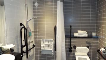 A modern bathroom with a shower, toilet, and bidet, equipped with grab bars and a hand dryer.