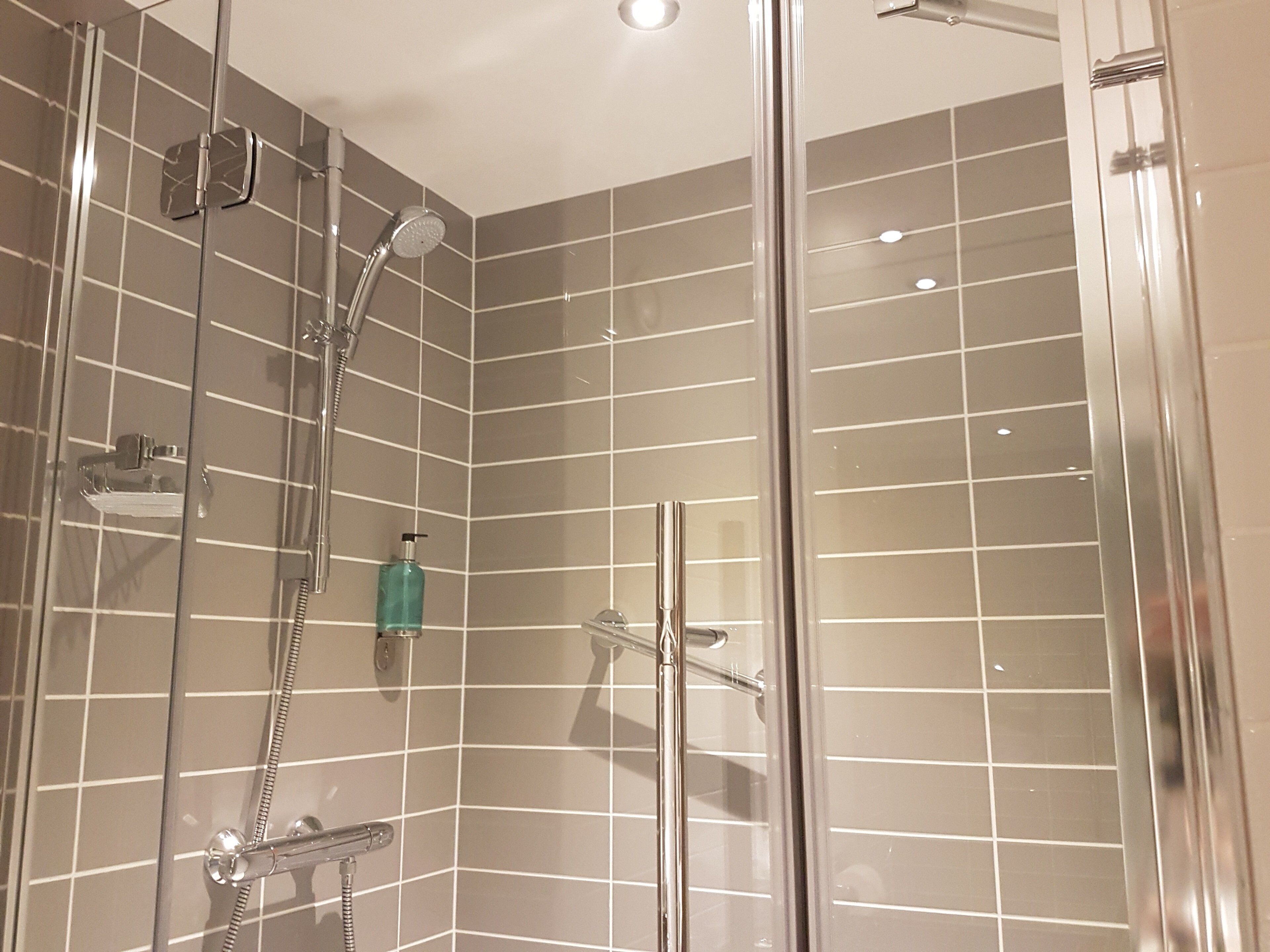 A glass-enclosed shower with a handheld showerhead and a wall-mounted faucet.