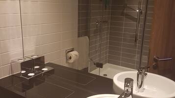 Une salle de bain moderne avec un plan de toilette noir, deux vasques blanches, une cabine de douche en verre et un porte-rouleau de papier toilette.