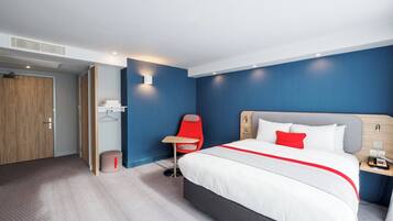Una habitación de hotel moderna con una cama grande, una silla roja, una mesita pequeña y una mesita de noche de madera.