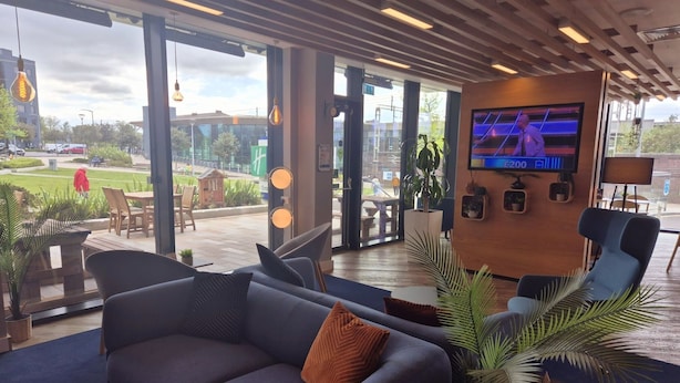 Un salon moderne comprenant un canapé, des fauteuils, un téléviseur et de grandes fenêtres donnant sur un paysage urbain.
