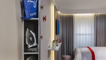 A hotel room with a bed, a wardrobe, a hairdryer, a small table with toiletries, and a window with curtains.