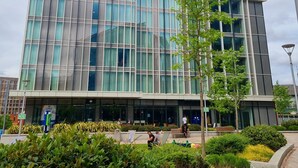Un bâtiment moderne doté de grandes fenêtres, une enseigne indiquant un hôtel Holiday Inn Express, et un espace paysager agrémenté de bancs et d’arbres.