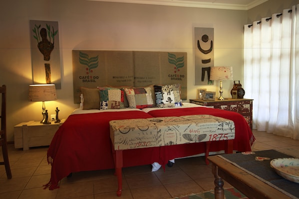 A hotel room with a large bed, a nightstand with a lamp, a wooden bench, and a wall with artwork and a sign.