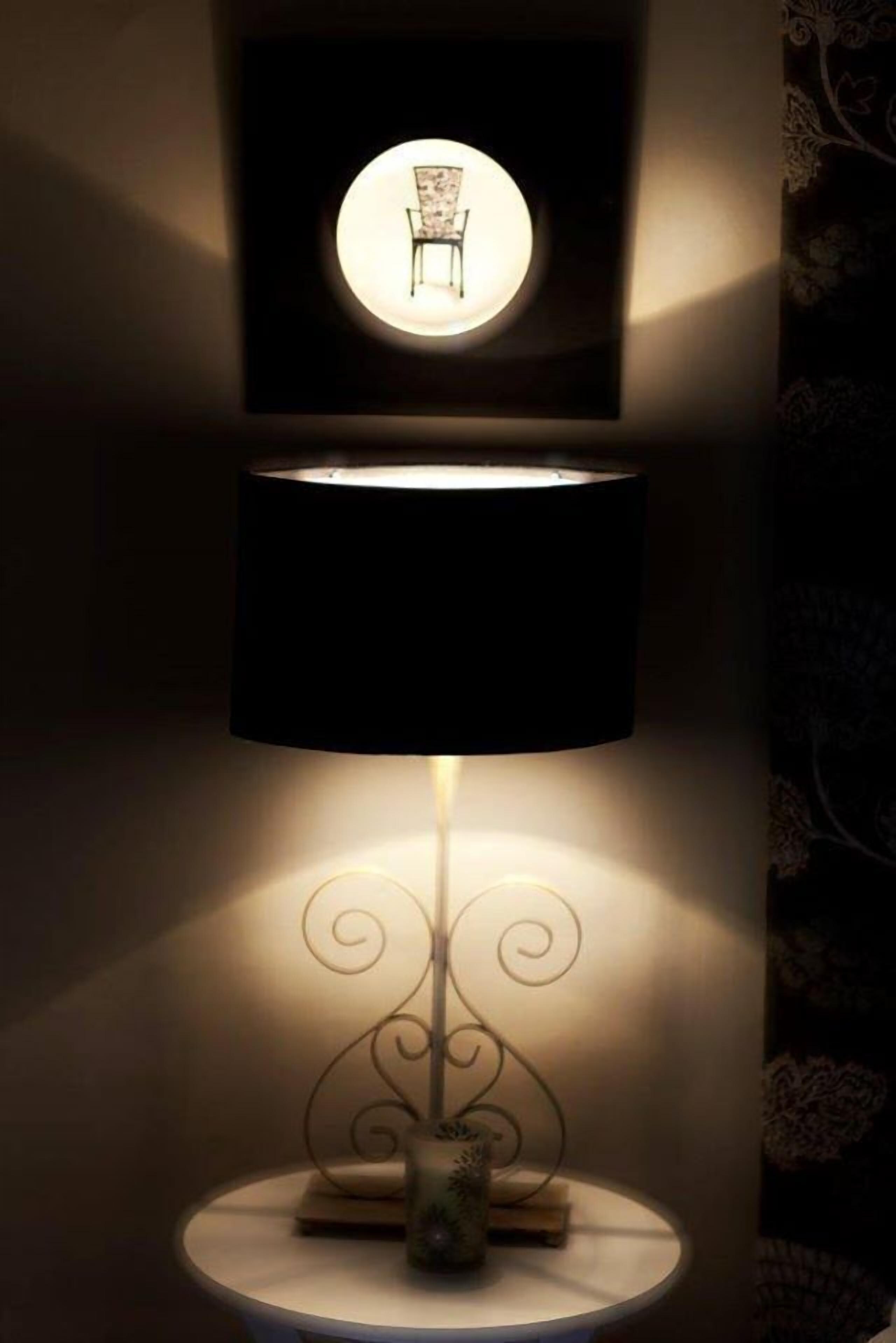 A floor lamp with a black shade and a decorative base, positioned on a round table.