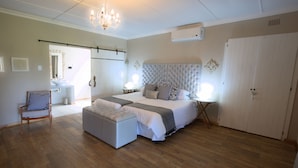 Une chambre à coucher avec un grand lit, un plancher en bois, un lustre, une table de chevet et une armoire.