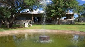 Une fontaine dans un bassin circulaire, avec une maison en arrière-plan.
