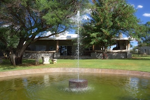 Uma fonte em um lago circular, com uma casa ao fundo.