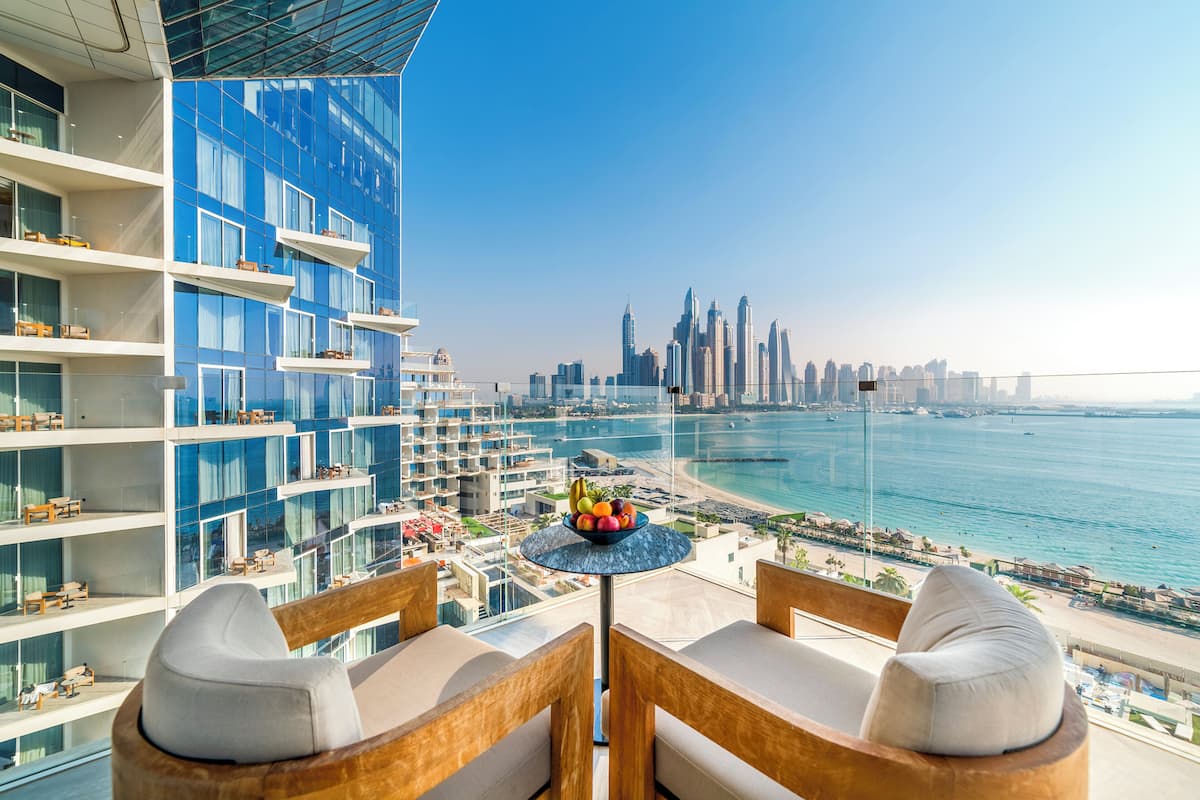 A balcony with a table holding fruit, overlooking a city skyline and a beach.
