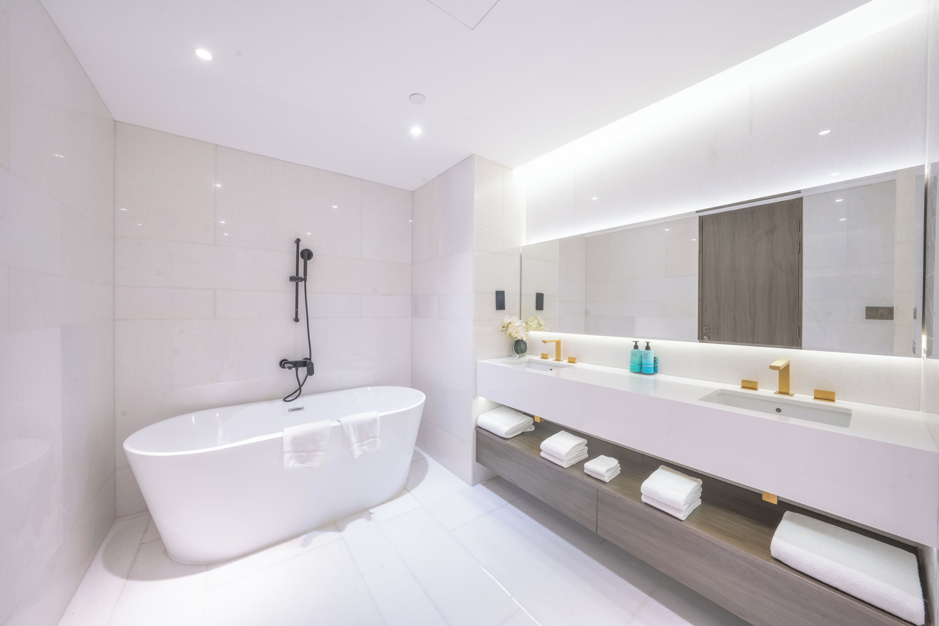 Un baño moderno con una bañera independiente, un espejo grande y un tocador con lavabo y toallero.