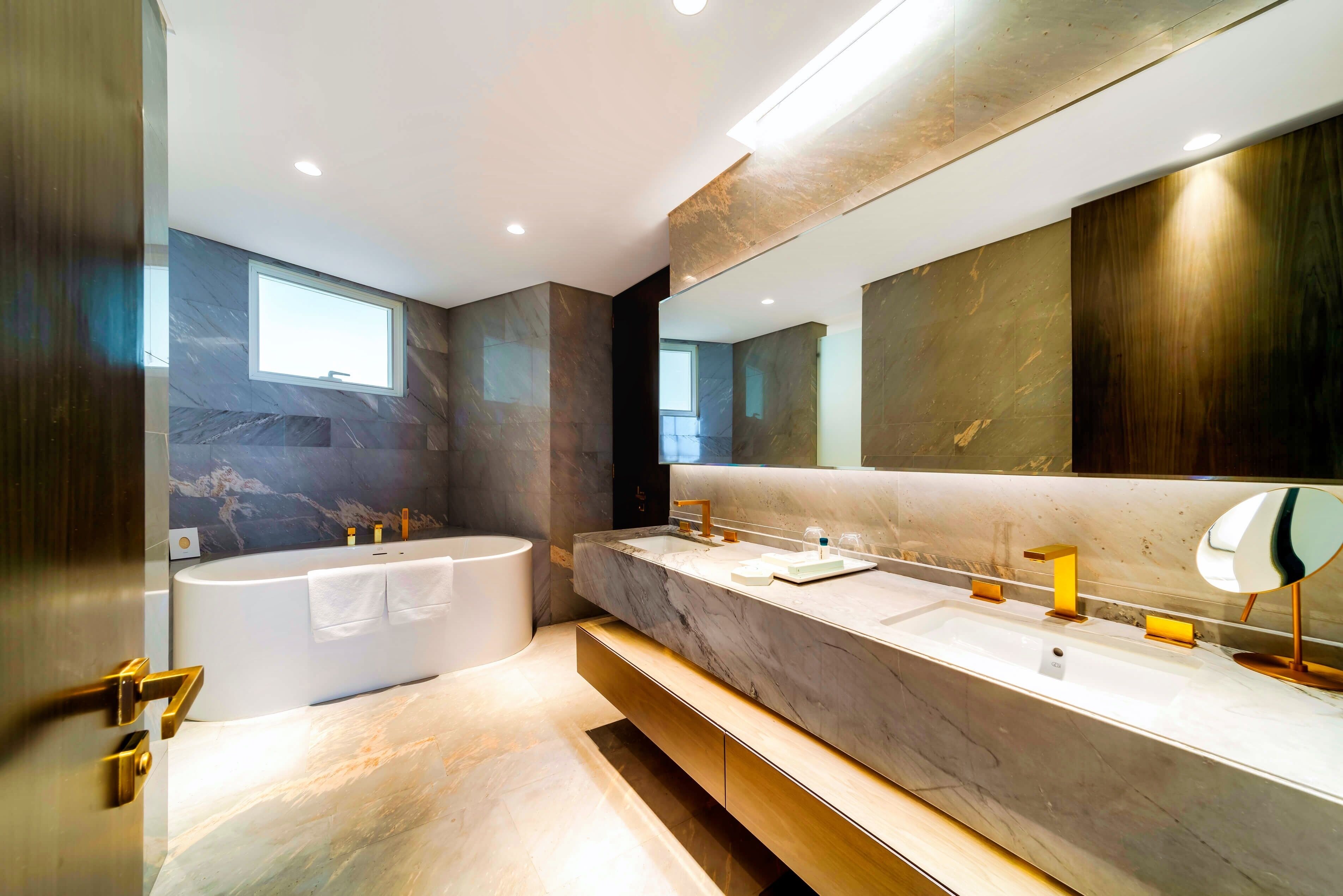 A modern bathroom with a large bathtub, a vanity with a mirror, and a window.