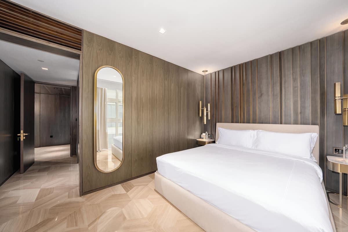 A modern hotel room with a large bed, a mirror, a bedside table, and a wall-mounted light fixture.