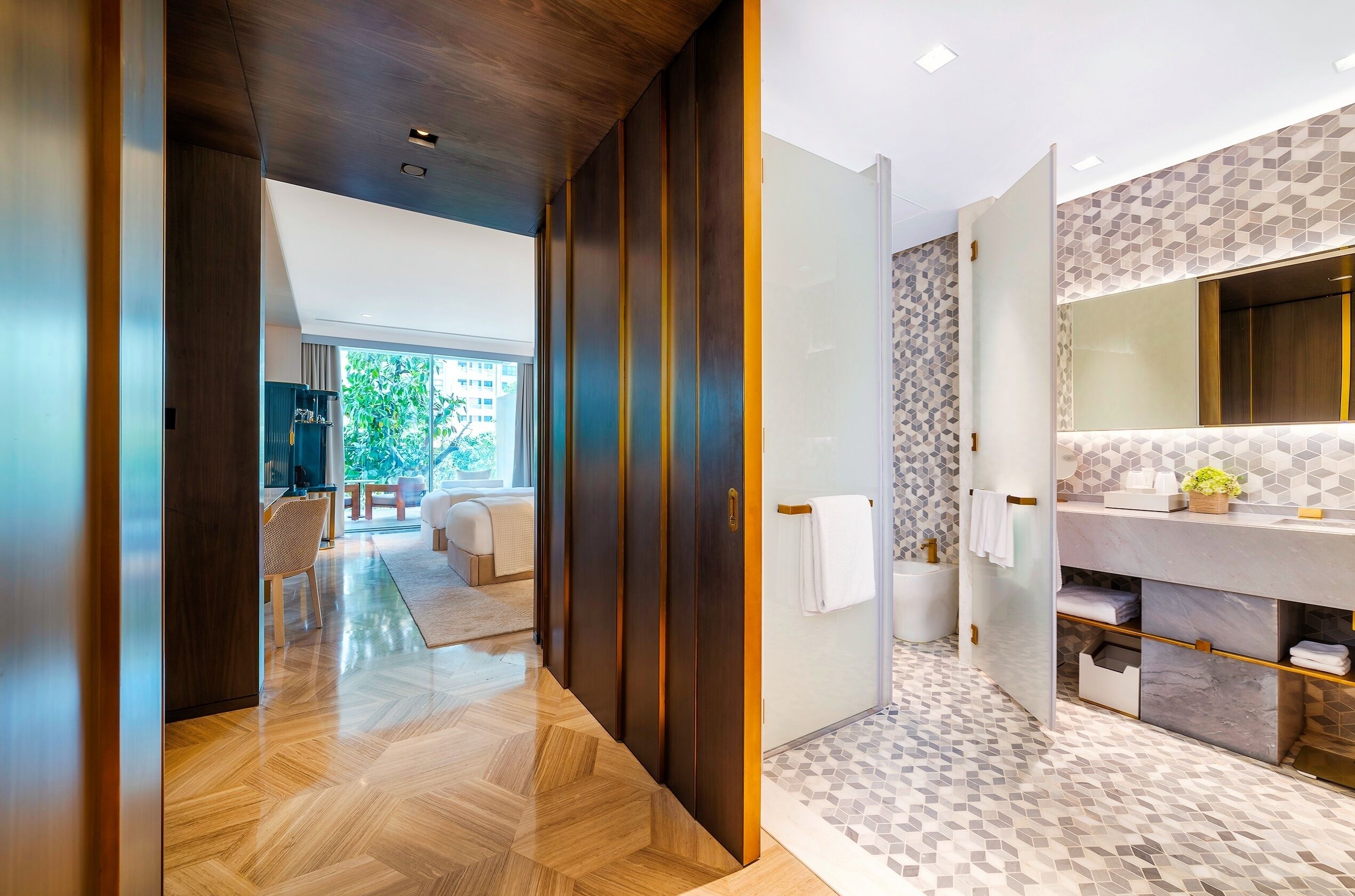 Une salle de bain moderne avec un grand miroir, des étagères en marbre et un sol orné d’un motif en chevrons.