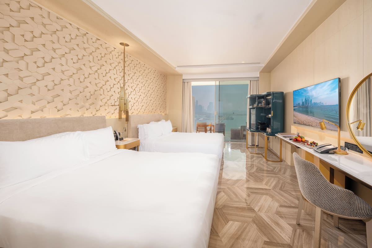 A hotel room with two beds, a desk with a chair, a television, and a large window with a city view.