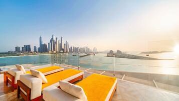 A rooftop lounge with yellow cushions and white sofas, overlooking a city skyline and a body of water.