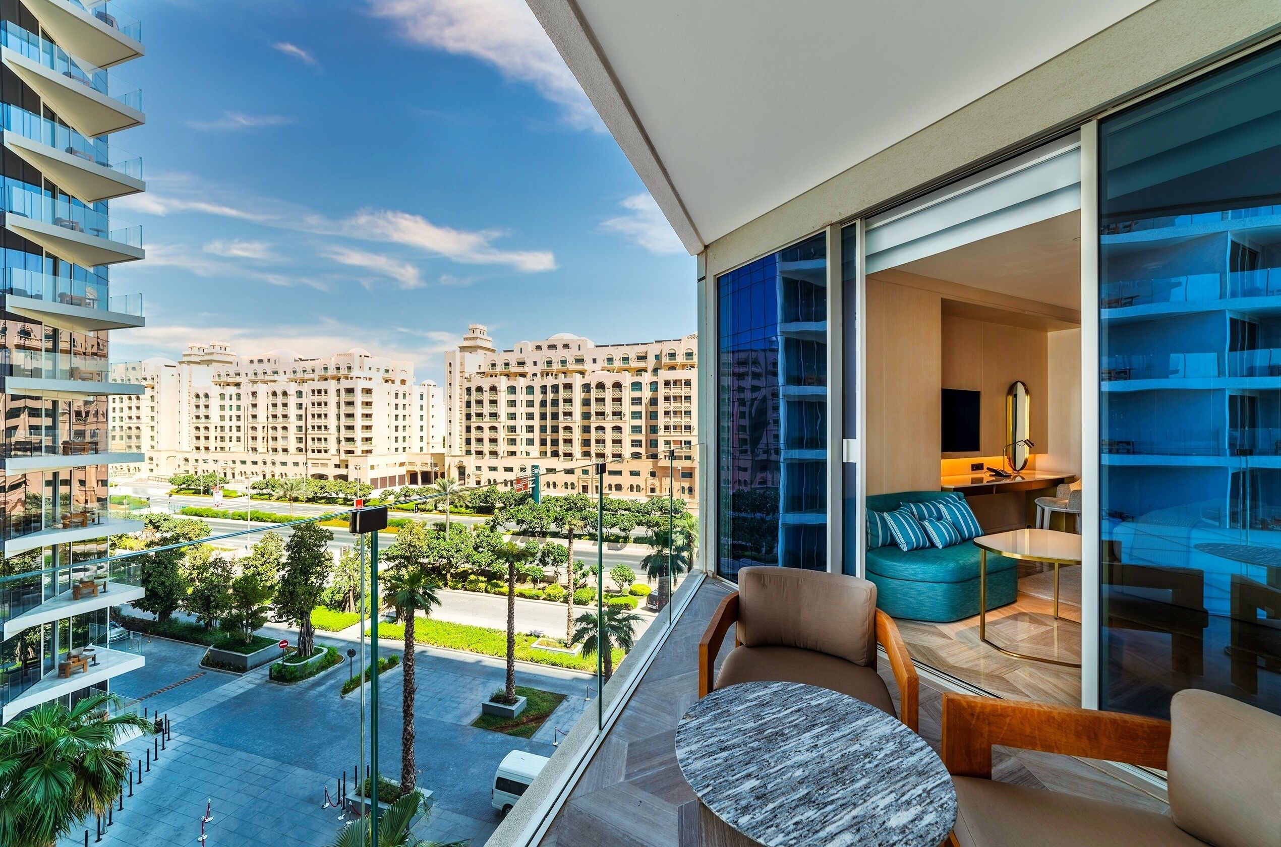 Une chambre d’hôtel moderne avec balcon, de grandes fenêtres et une vue sur le paysage urbain.