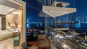 Een moderne hotelkamer met stadszicht, een balkon met glazen balustrade, en een ruime zithoek met een bank en een klein tafeltje.