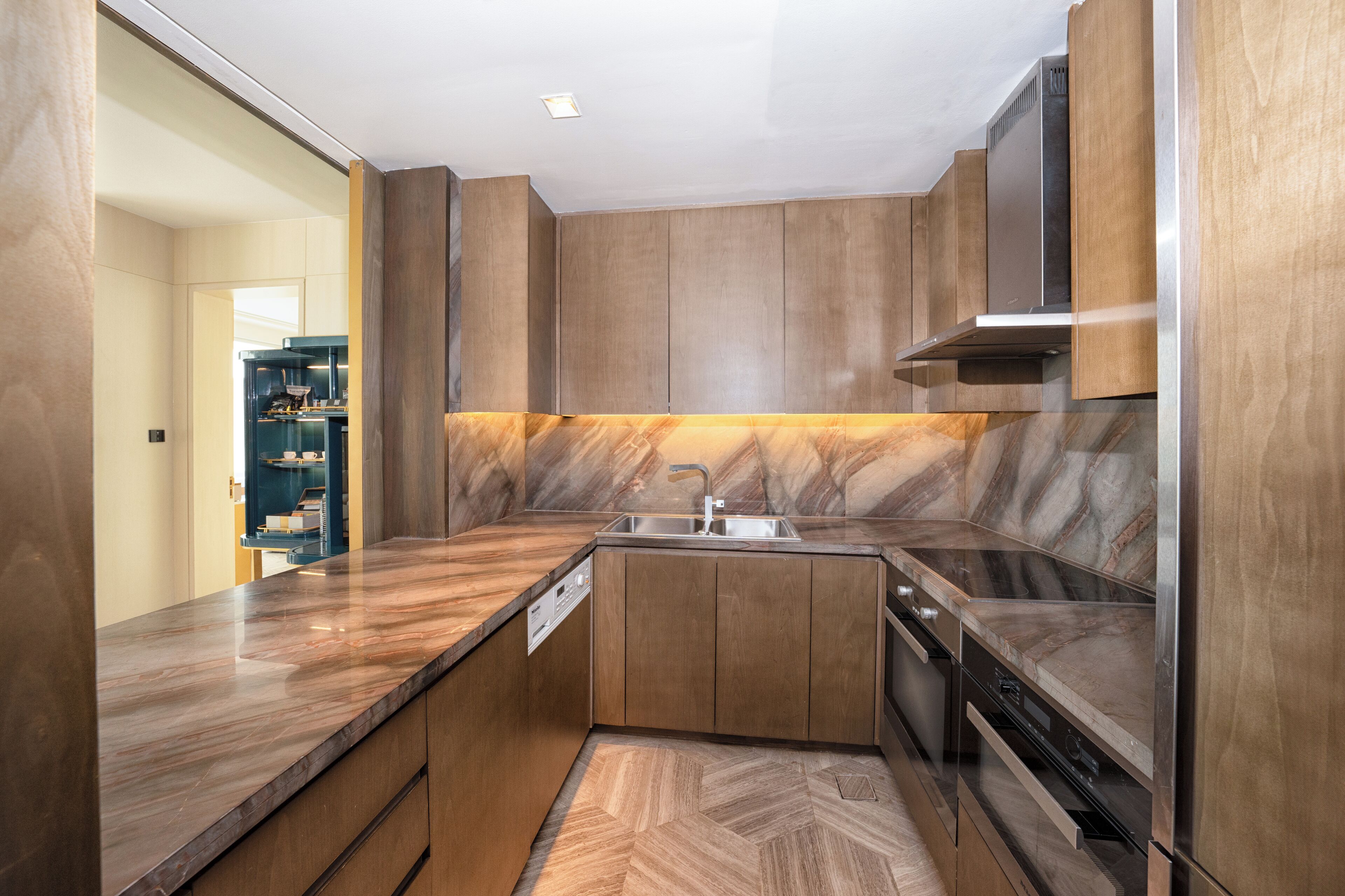 A compact kitchen with wooden cabinets, a marble countertop, and a built-in dishwasher.