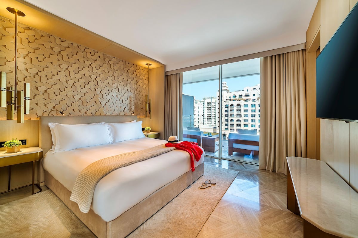 A modern hotel room with a large bed, a TV, a desk, and a balcony with a city view.