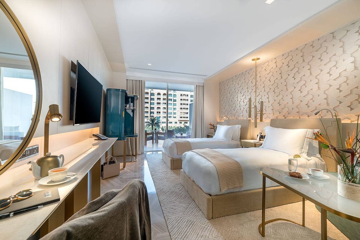 A hotel room with a large bed, a smaller bed, a desk with a chair, a TV, and a view of the city.