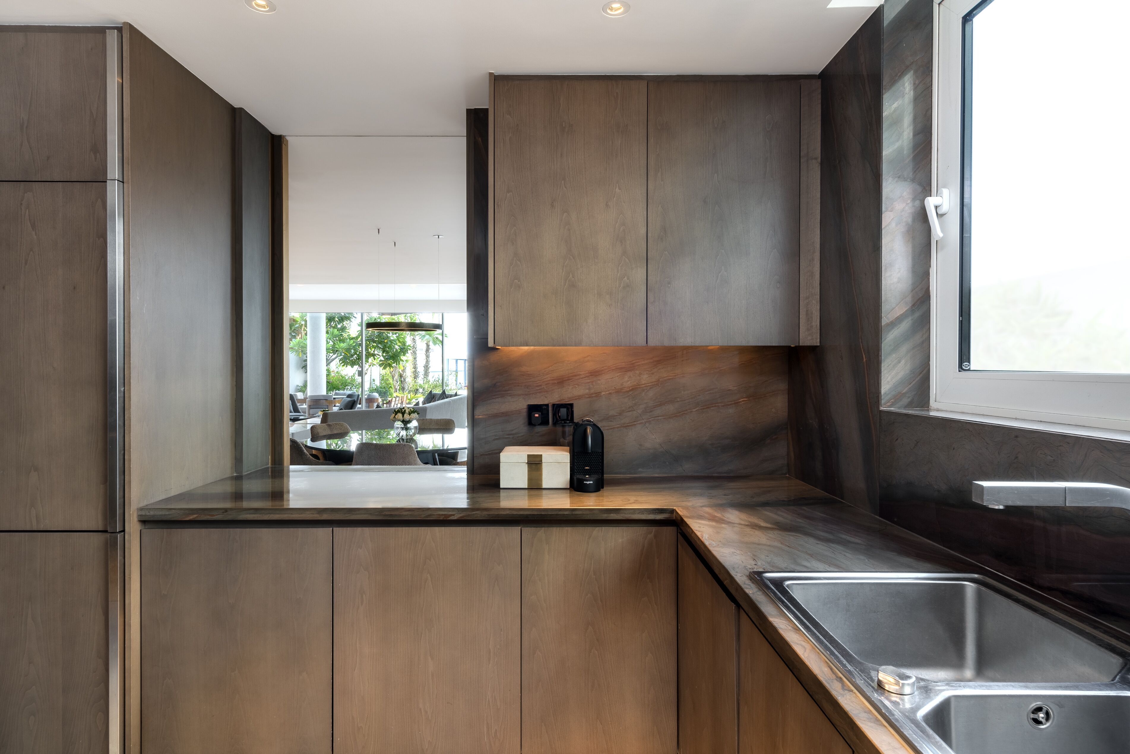 A modern kitchen with wooden cabinets, a built-in coffee maker, and a stainless steel sink.