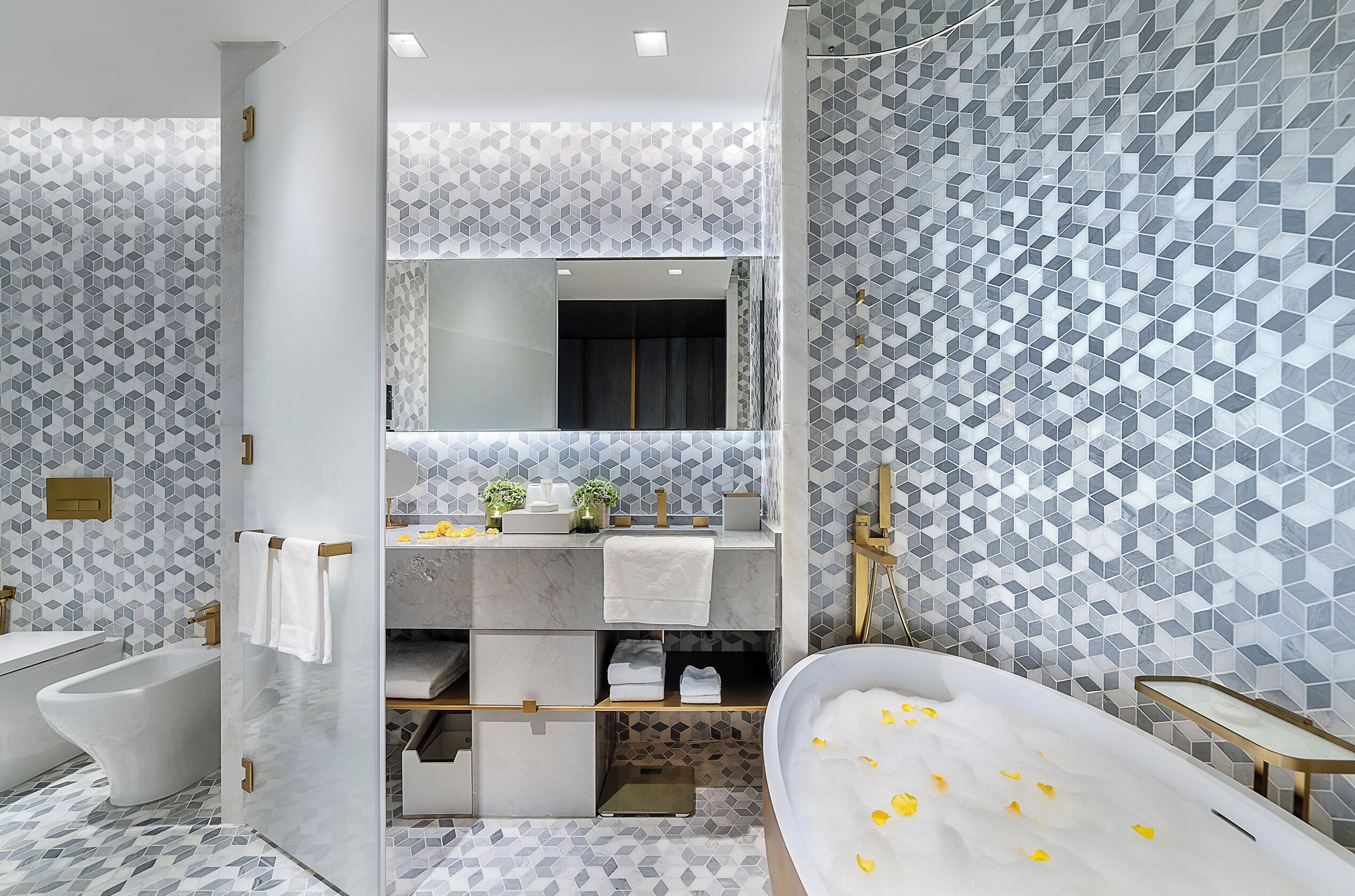 A modern bathroom with a freestanding bathtub, a large mirror, and a geometric tile pattern on the walls and floor.