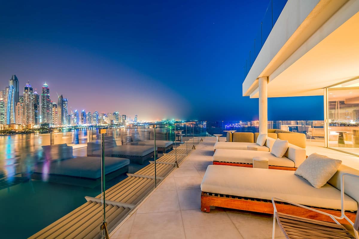 A rooftop lounge with a city view, modern furniture, and a glass railing overlooking the water.