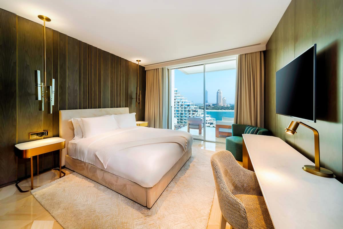 A modern hotel room with a large bed, a desk, a flat-screen TV, and a balcony with a city view.